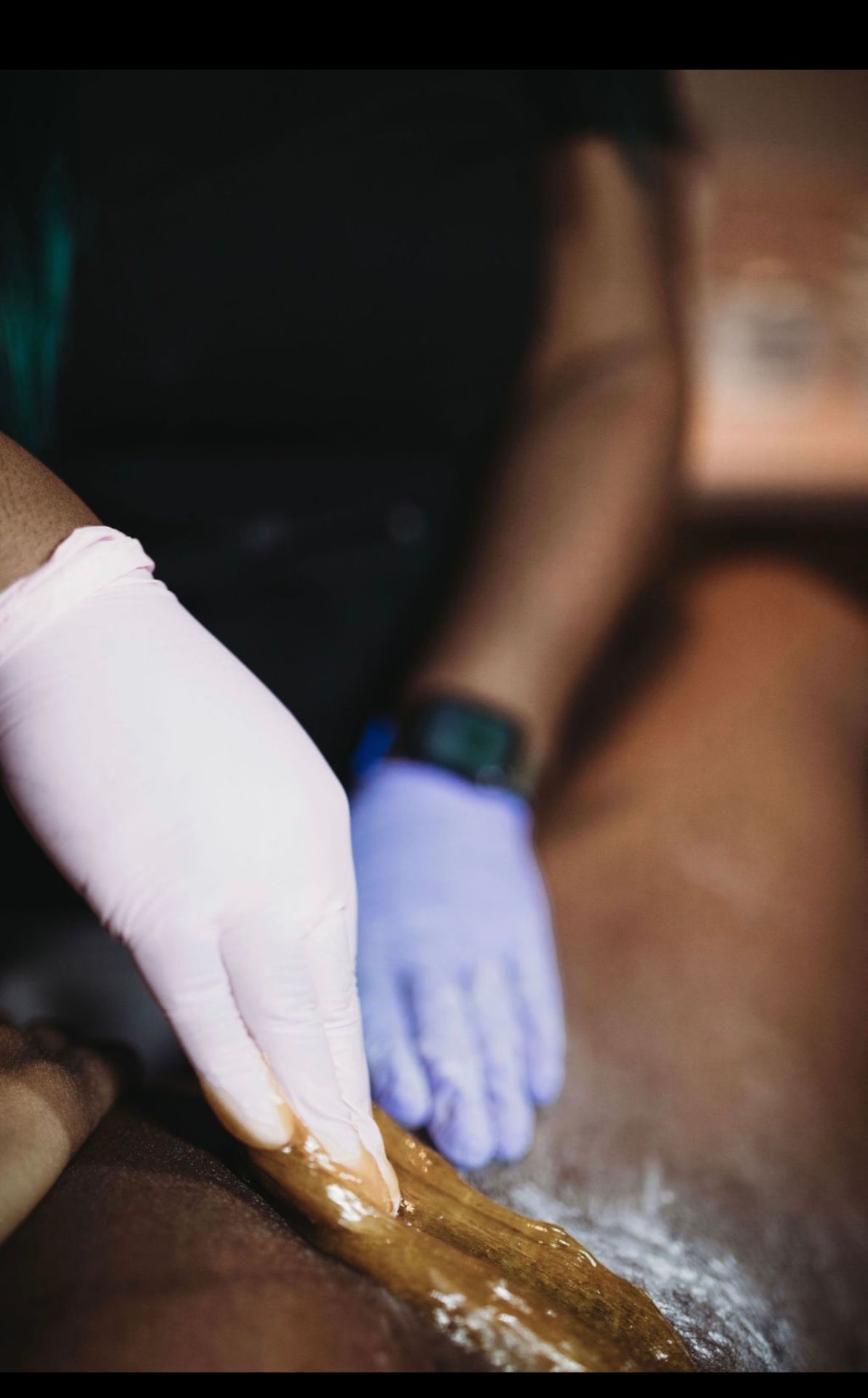 Esthetician flicking sugar paste in the direction of hair growth on a client's leg